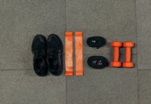 Flat lay of gym essentials including dumbbells, sneakers, and resistance bands on a grey floor.