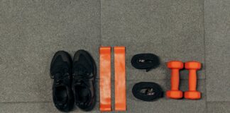 Flat lay of gym essentials including dumbbells, sneakers, and resistance bands on a grey floor.