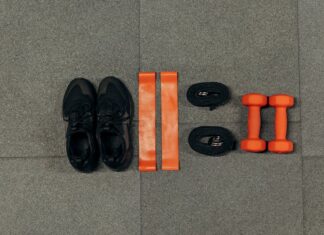Flat lay of gym essentials including dumbbells, sneakers, and resistance bands on a grey floor.