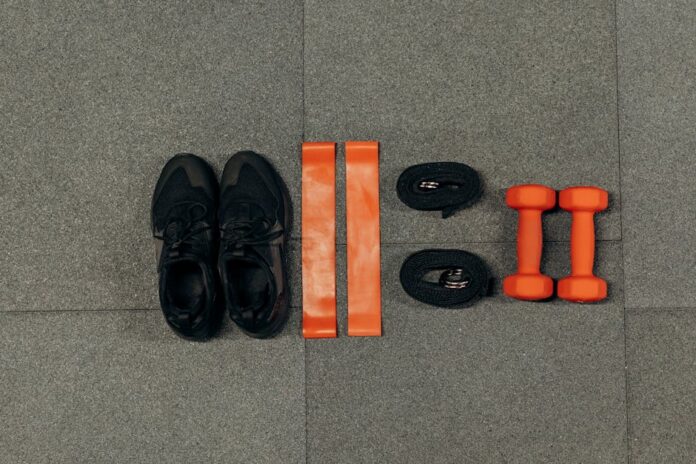 Treino Simples para Perder Peso: Descubra o Segredo Eficaz! Flat lay of gym essentials including dumbbells, sneakers, and resistance bands on a grey floor.