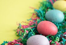 Atividades físicas para fazer na Páscoa: Inove o seu feriado Vibrant Easter eggs lying on colorful shredded paper, perfect for spring celebrations.