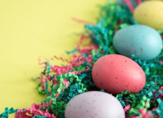 Atividades físicas para fazer na Páscoa: Inove o seu feriado Vibrant Easter eggs lying on colorful shredded paper, perfect for spring celebrations.