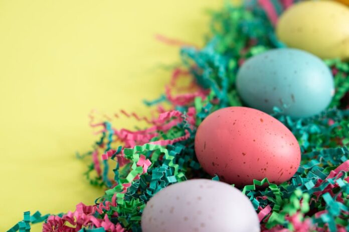 Atividades físicas para fazer na Páscoa: Inove seu feriado! Vibrant Easter eggs lying on colorful shredded paper, perfect for spring celebrations.