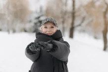 Como manter a forma no inverno: Dicas surpreendentes Elderly woman wearing a winter jacket and cap stretches arms outdoors in a snowy park.