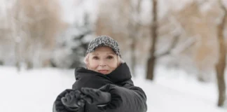 Como manter a forma no inverno: Dicas surpreendentes Elderly woman wearing a winter jacket and cap stretches arms outdoors in a snowy park.