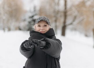 Como manter a forma no inverno: Dicas surpreendentes Elderly woman wearing a winter jacket and cap stretches arms outdoors in a snowy park.