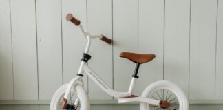 A white kids' balance bike with brown accents standing indoors against a wooden wall.