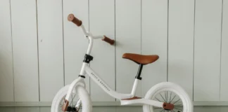 Descubra as melhores ciclovias para iniciantes no Brasil A white kids' balance bike with brown accents standing indoors against a wooden wall.