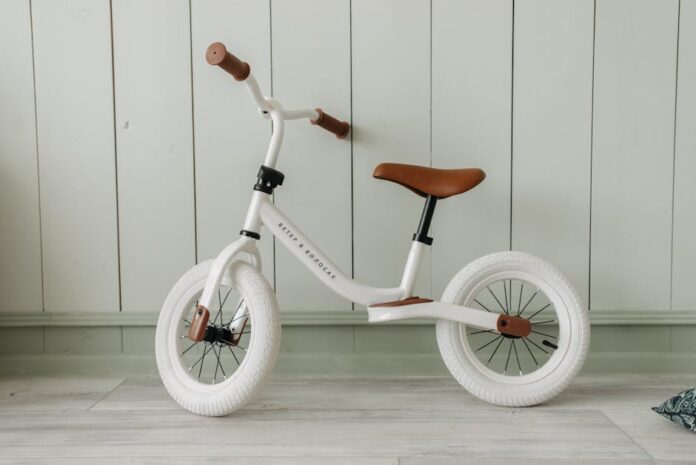 Descubra as Melhores Ciclovias para Iniciantes no Brasil A white kids' balance bike with brown accents standing indoors against a wooden wall.