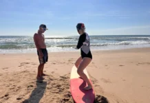 Desporto para séniores iniciantes: Dicas surpreendentes A woman learning to surf with an instructor on a sunny beach day.