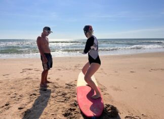 Desporto para séniores iniciantes: Dicas surpreendentes A woman learning to surf with an instructor on a sunny beach day.