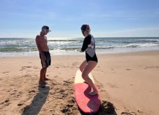 Desporto para séniores iniciantes: Dicas surpreendentes A woman learning to surf with an instructor on a sunny beach day.