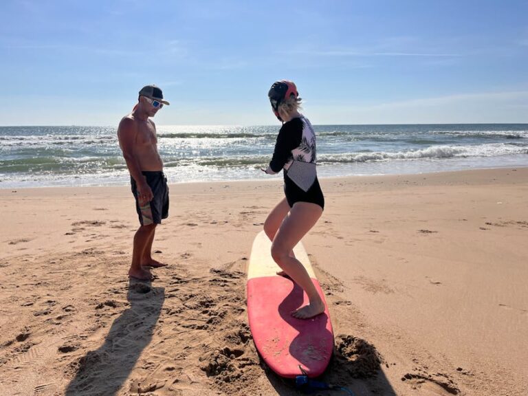 A woman learning to surf with an instructor on a sunny beach day.