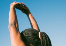 Dieta e exercício antes do verão: Surpreenda-se com os resultados Person stretching outdoors with braided hair against a clear blue sky for a healthy lifestyle concept.