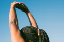 Dieta e exercício antes do verão: Surpreenda-se com os resultados Person stretching outdoors with braided hair against a clear blue sky for a healthy lifestyle concept.