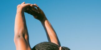 Dieta e exercício antes do verão: Surpreenda-se com os resultados Person stretching outdoors with braided hair against a clear blue sky for a healthy lifestyle concept.