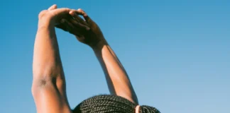 Dieta e exercício antes do verão: Surpreenda-se com os resultados Person stretching outdoors with braided hair against a clear blue sky for a healthy lifestyle concept.