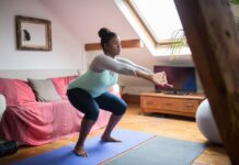 Personal Trainer ao domicílio A woman performs squats on a yoga mat in a cozy living room, promoting home fitness and wellness.