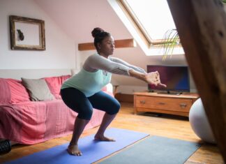 Personal Trainer ao domicílio A woman performs squats on a yoga mat in a cozy living room, promoting home fitness and wellness.