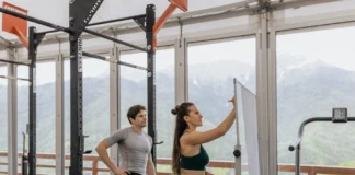 Plano de treino para o Verão: Surpreenda-se com os resultados A gym coach instructs on whiteboard beside fitness equipment with mountain view.