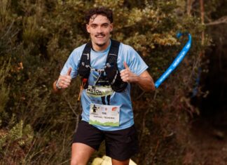 Provas de Trail Running: Descubra as rotas mais desafiadoras Young male trail runner enthusiastically giving a thumbs up during an outdoor race through forest.