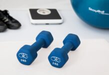 Blue dumbbells placed on a white surface with fitness equipment in the background.