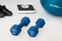 Treino em casa nos dias de chuva: Transforme o seu espaço Blue dumbbells placed on a white surface with fitness equipment in the background.