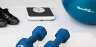 Treino em casa nos dias de chuva: Transforme o seu espaço Blue dumbbells placed on a white surface with fitness equipment in the background.