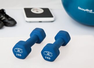Treino em casa nos dias de chuva: Transforme o seu espaço Blue dumbbells placed on a white surface with fitness equipment in the background.
